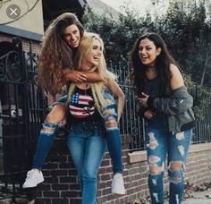 three young women standing next to each other in front of a brick wall and gate