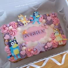 a birthday cake with pink frosting and cartoon characters on it sitting in a box