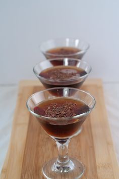 three glasses filled with liquid sitting on top of a wooden tray