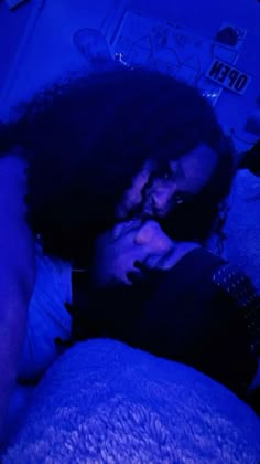 a man and woman laying in bed with blue lights on their faces, one is holding the other's head