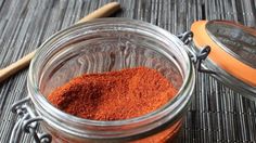 a jar filled with red spices next to a wooden spoon on top of a table