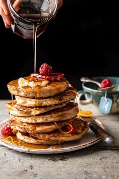 a stack of pancakes with syrup being drizzled over them and topped with raspberries