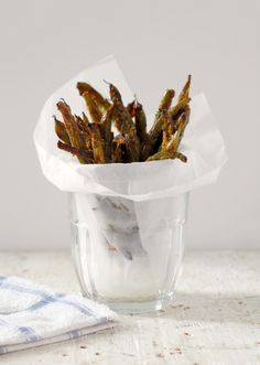 a glass vase filled with dried grass on top of a white tablecloth next to a blue and white towel