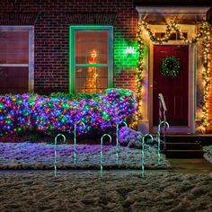 christmas lights decorate the front yard of a brick house with candy canes in front