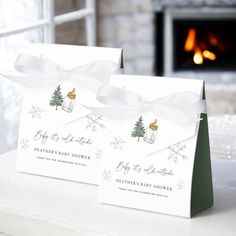 two christmas gift bags sitting on top of a white table next to a fire place