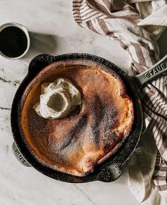 a pie with whipped cream on top sits in a skillet next to a cup of coffee