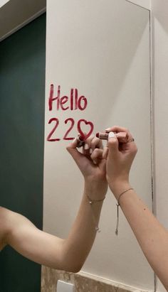 two people are writing on a wall with red marker and white paper that says hello 223