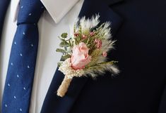 a boutonniere with pink flowers and feathers on a man's lapel