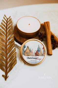 a candle and some cinnamon sticks on a white table with a gold leaf next to it