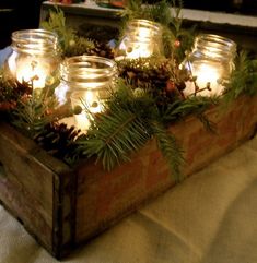 mason jars filled with pine cones and candles sit in a wooden box on a table