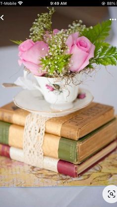 pink roses are in a teacup on top of three books, sitting on a table