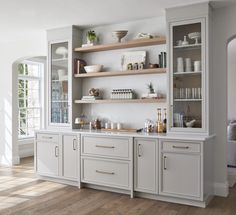 a kitchen with white cabinets and shelves filled with dishes on top of wooden flooring