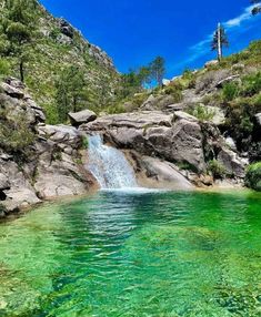 the water is green and clear with some rocks on either side that has a waterfall coming out of it