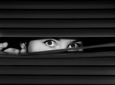 a woman peeking out from behind blinds with her eyes wide open