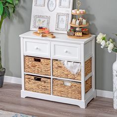 a white dresser with wicker baskets and pictures on the top, next to a potted plant