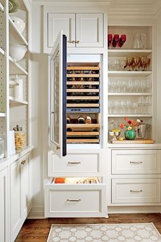 a kitchen with white cupboards and drawers filled with wine glasses, dishes and utensils