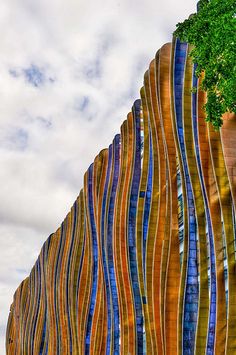 a building made out of multicolored glass and wood with a tree in the foreground