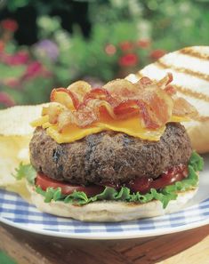 a hamburger with bacon, lettuce and tomato on it sitting on a plate