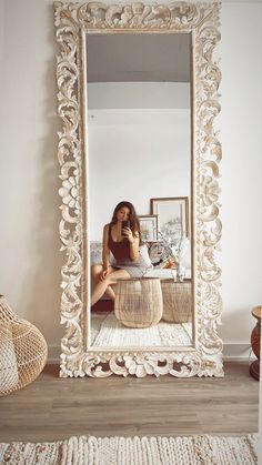 a woman taking a selfie in front of a large mirror with shells on the floor