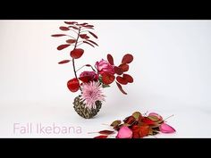 a vase filled with red and pink flowers on top of a white table next to dried leaves