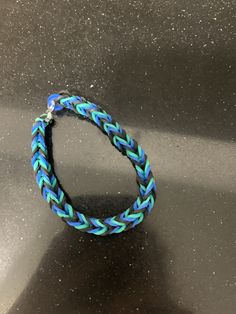 a blue and green braided bracelet sitting on top of a black counter next to a cell phone