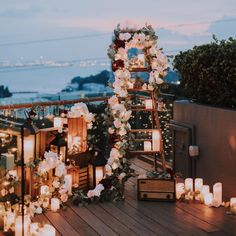 an outdoor wedding setup with candles and flowers on the deck overlooking the water at dusk