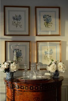 three framed pictures on the wall above a table with vases and flowers