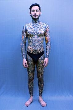 a man with tattoos on his body standing in front of a blue background