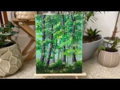 an easel with a painting of trees in the middle and potted plants behind it