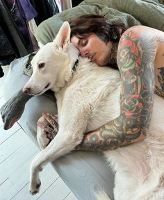 a tattooed woman laying on top of a white dog