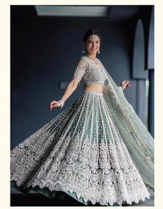 a woman in a white and green lehenga is standing with her arms outstretched