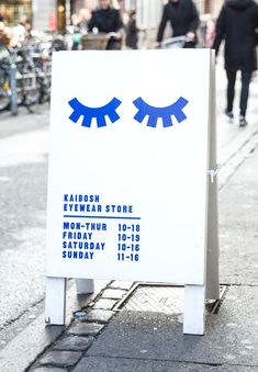 a white sign with blue eyes on the side and people walking down the street in the background