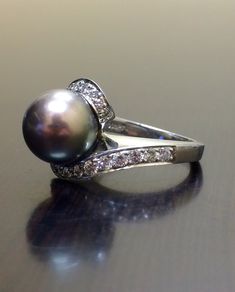 DeKara Designs Collection Beautiful Art Deco/Vintage/Modern Style Pearl Engagement Ring. Metal- 18K White Gold, .750. Stones- 10 MM Round Tahitian/South Sea Black Pearl, 24 Round Diamonds, F-G color VS1 clarity, 0.62 Carats. The ring is beautiful with a unique Tahitian pearl that is round in shape. This pearl changes from champagne brown, to a purple bronze color. This is a fantastic pearl that is also rare to find. The diamond has two rows of pave set diamonds that are graduating from big to sm Platinum Diamond Wedding Ring, Black Pearl Ring, Pearl Diamond Ring, Pearl Wedding Ring, Vintage Modern Style, Pearl Engagement Ring, Black Engagement Ring, Tahitian Black Pearls, Pearl And Diamond Ring