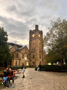 two people are sitting on a bench in front of a building with a clock tower