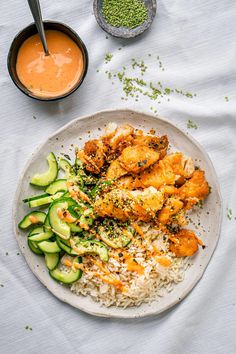 a white plate topped with rice and veggies next to a bowl of sauce