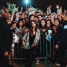 a large group of people standing in front of a metal barricade at night