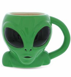 a green coffee mug with an alien face on it's side and black eyes