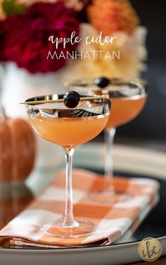 an apple cider manhattan cocktail is garnished with black olives and served in coupe glasses