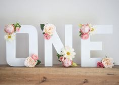 the word one is decorated with flowers on top of a wooden shelf in front of a white wall