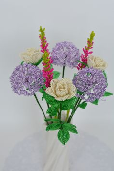 a white vase filled with lots of purple and white flowers on top of a table