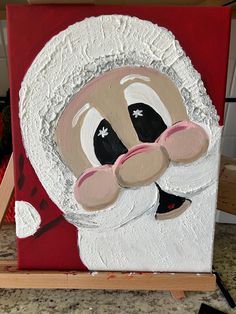 a close up of a painting of santa claus on a easel with paintbrushes