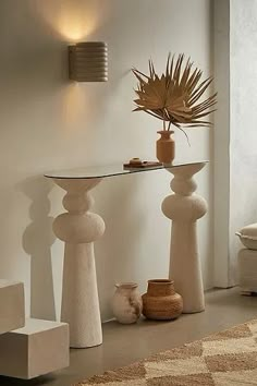 a table with vases and plants on it in front of a white wall next to stairs