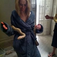 a woman in a bathrobe holding a snake wrapped around her body and wearing sandals