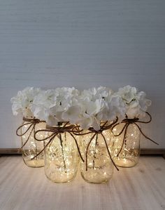 four mason jars filled with white flowers and string lights