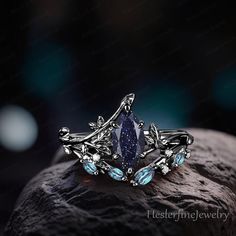 a ring with blue stones and leaves on top of a rock in front of a dark background