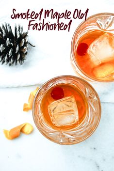 two glasses filled with drinks sitting on top of a white counter next to a pine cone