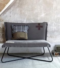 a grey couch sitting in front of a stone wall with a cross on the pillow