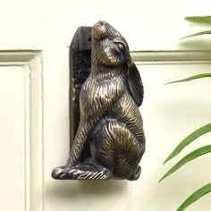 a bronze colored bear door knocker on a white wall next to a potted plant