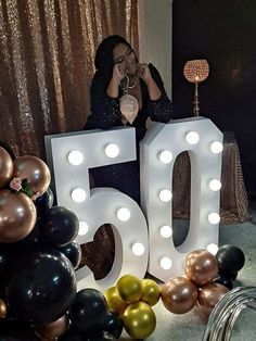 a woman sitting in front of the number 50 surrounded by balloons