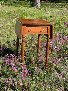 a small wooden table sitting on top of a lush green field filled with purple flowers